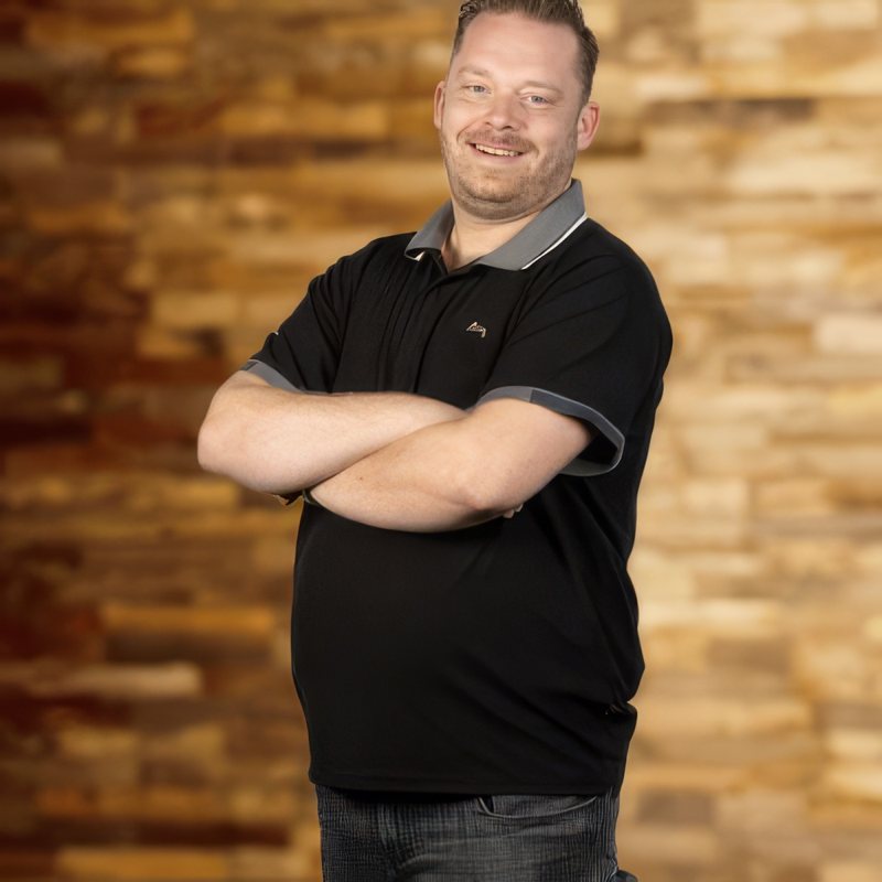 De eigenaar van JVDH Installatie, met gekruiste armen voor een houten wand